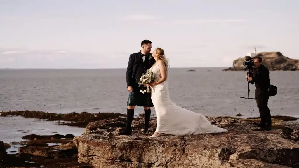 scotland wedding videographer filming a couple on a rock overlooking a view of the sea near North Berwick