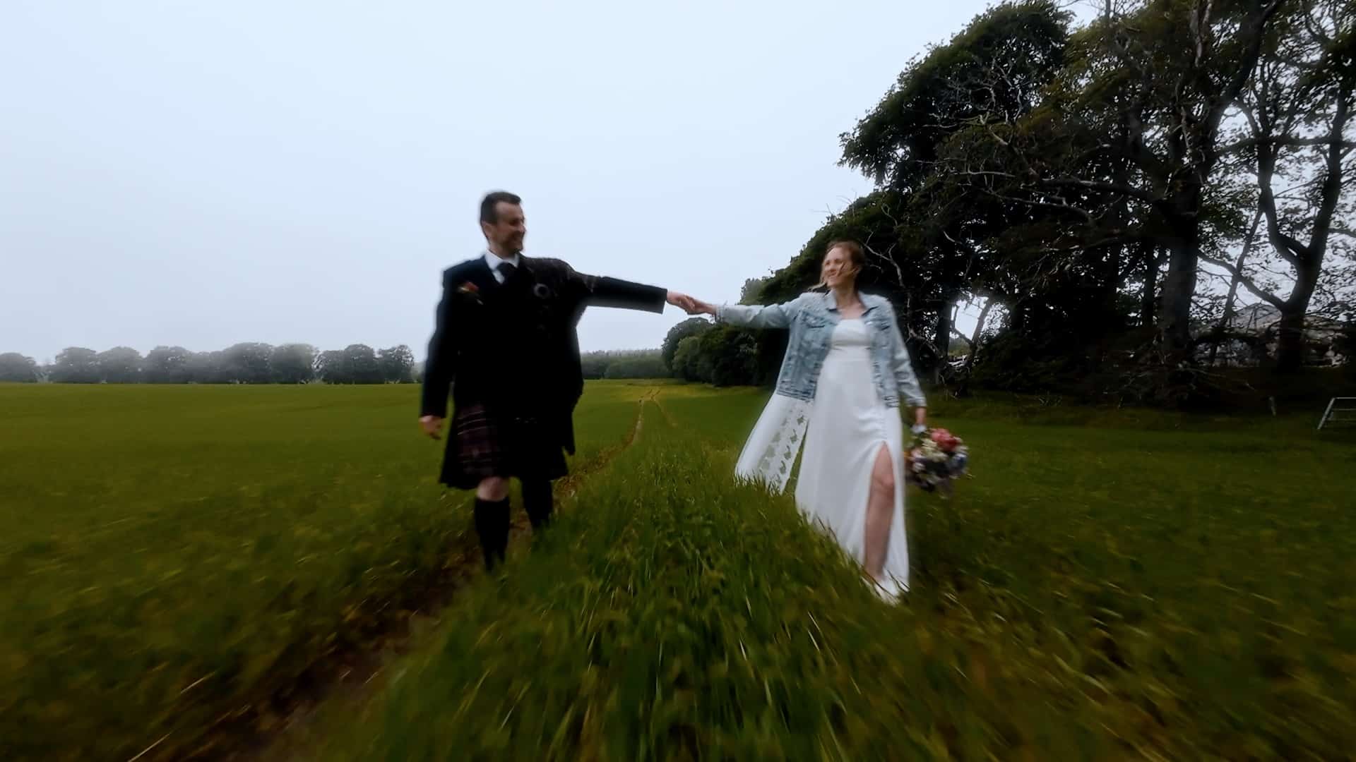 bride and groom holding hands in cornfield on their wedding day. Overcast day with green grass int he field