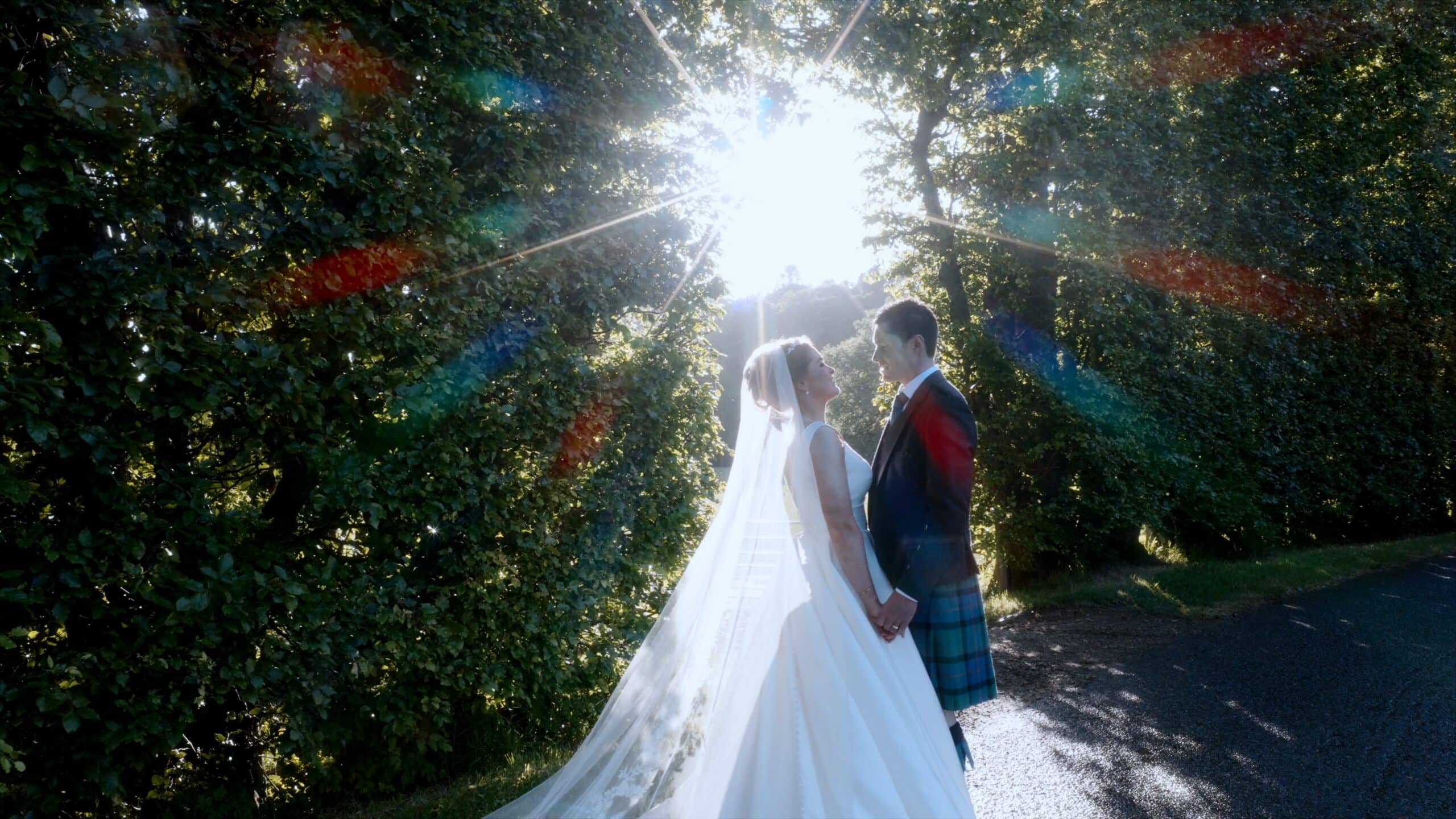 Nicola and Davy posing in front of a hedge at Aswanley wedding venue with sun coming through the trees behind them