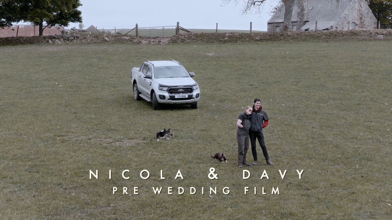 nicola and davy looking out at the view on top of their farm. Photo is taken from a drone showing their truck and two dogs in the background.